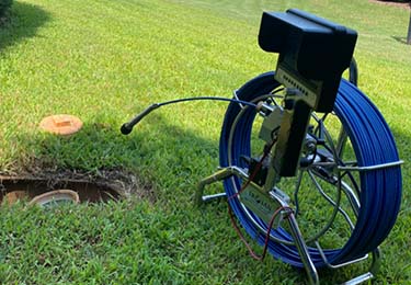 A picture of a sewer scope device, sitting next to the access point of a sewer line ready for inspection.